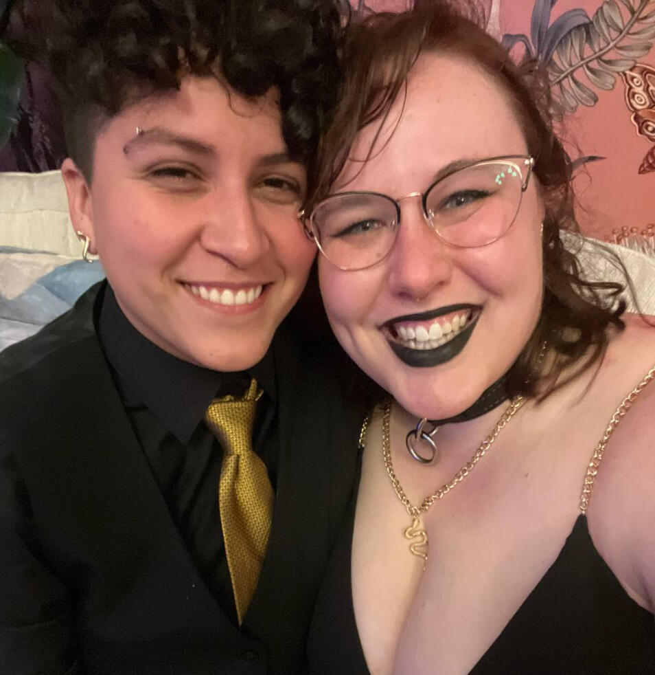 Rooster, on left, smiling while wearing black suit with gold tie. Sol, on right, smiling while wearing black dress with gold jewelry.